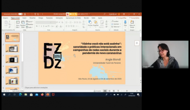 Imagem da transmissão ao vivo do evento Fazendo e Desfazendo Gênero. À esquerda, slides com o logo do evento e o título do trabalho de pesquisa: &quot;Vizinha você não está sozinha: sororidade e práticas interacionais em campanhas de redes sociais durante a pandemia do novo coronavírus&quot;. À direita, a imagem da pesquisadora Angie Biondi faz a apresentação. Ela é uma mulher de pele branca, cabelos escuros na altura do pescoço e óculos de aro vermelho. 