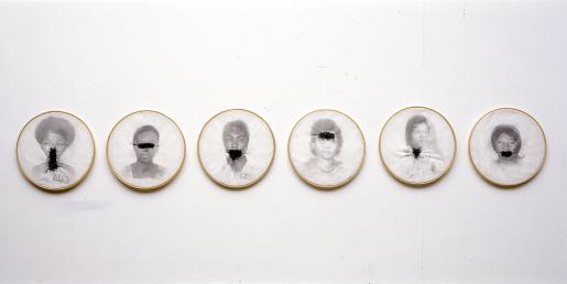 Foto de seis bastidores, armações circulares utilizadas para fazer bordados em tecidos. Cada um deles traz a reprodução de uma fotografia em preto e branco de diferentes mulheres negras, e em cada bastidor a mulher retratada tem uma parte diferente do rosto ou pescoço coberta por um bordado grosseiro feito com linha preta.