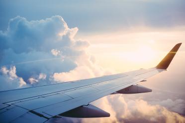Foto colorida em ambiente externo, da asa de um avião em contraste com o céu e as nuvens.