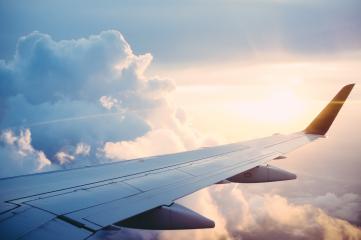 Foto colorida em ambiente externo, de um avião voando acima das nuvens.