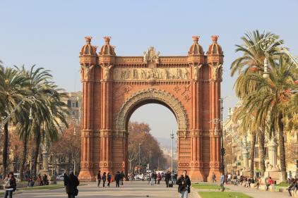 Imagem colorida em ambiente externo, de uma praça com um arco de concreto cruzando-a, sendo o Arco do Triunfo em Barcelona.
