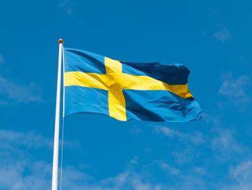 Foto colorida, em ambiente externo, de bandeira da Suécia hasteada sob céu azul
