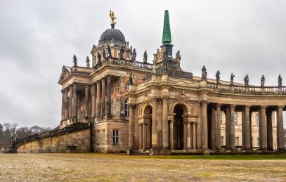 Foto colorida, em ambiente externo, do Novo Palácio de Potsdam, que conta com inúmeras colunas e estátuas no telhado