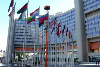 Foto colorida em ambiente externo, de bandeiras de vários países hasteadas em frente a um prédio.