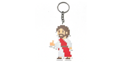 Foto de chaveiro com a ilustração pixelada de Jesus fazendo sinal de jóia. Jesus é retratado como um homem branco de cabelos e barba castanhos, vestindo uma túnica branca com uma faixa vermelha. O fundo é branco.