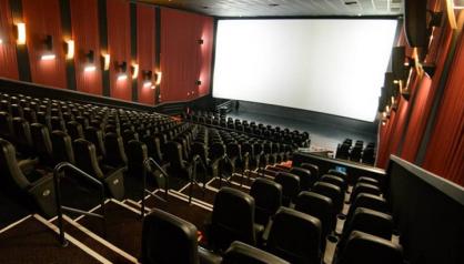 Foto tirada nas últimas fileiras de uma sala de cinema. As luzes estão acesas, mas não há ninguém nas poltronas e nada é exibido na tela.