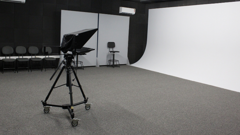 Equipamento de gravação do estúdio de TV, montado em tripé; ao lado, fundo infinito, na cor branca - abril de 2022