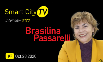 num fundo preto, aparecem, à direita, uma imagem da entrevistada (uma mulher branca, de cabelos curtos e loiros, que veste um blazer amarelo e uma blusa roxa. Do lado esquerdo, está escrito o nome da entrevistada, a data da entrevista e o nome do canal.