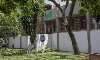 Fotografia do Departamento de Artes Plásticas. O prédio é branco. Uma escada liga o prédio a um gramado. Sobre a escada, na parede do prédio, uma placa verde indica o departamento. À frente do prédio há algumas árvores.