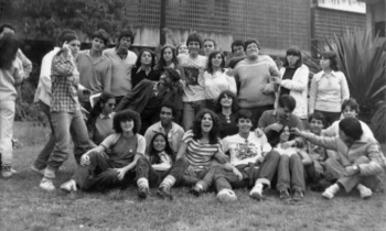 Foto em preto e branco mostra diversos jovens, homens e mulheres, no gramado em frente à fachada do prédio principal da ECA. Alguns estão sentados, enquanto outros estão atrás, de pé. A maioria sorri posando para a câmera e abraçando os colegas, enquanto outros estão distraídos no momento da foto. Alguns ainda fazem brincadeiras com os colegas. 