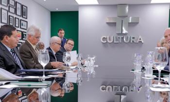 Foto do vice-presidente da República Hamilton Mourão sentado à mesa com diversos homens. Todos são brancos e têm cabelos grisalhos, à exceção de Mourão, que tem cabelos escuros e pele mais escura. Na parede ao fundo a logomarca da TV Cultura. 