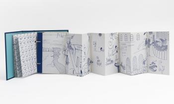 Foto de livro com capa azul e páginas brancas que se abrem em sanfona. Nas páginas, há diversos desenhos aparentemente feitos em caneta azul. O fundo é branco. 