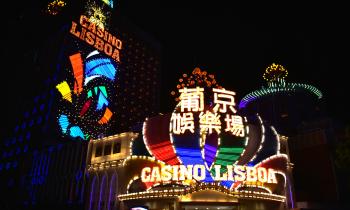 Foto de um Cassino em Macau. A fachada do local é iluminada e tem um letreiro que traz o nome “Casino Lisboa” junto a ideogramas chineses. As luzes coloridas do local contrastam com a noite escura.