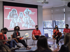 Foto de seis diretores da ECA Jr., homens e mulheres, sentados em frente à projeção com uma foto da equipe gestora. Eles vestem a camiseta vermelha da empresa.  No canto inferior da imagem, alguns estudantes assistem a apresentação.  Todos usam máscaras.