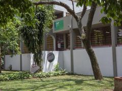 Fotografia do Departamento de Artes Plásticas. O prédio é branco. Uma escada liga o prédio a um gramado. Sobre a escada, na parede do prédio, uma placa verde indica o departamento. À frente do prédio há algumas árvores.