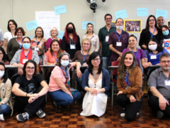 Foto de grupo de funcionárias e funcionários da ECA posando; à frente, as funcionárias estão sentadas; atrás delas outras funcionárias estão sentadas em carteiras escolares; ao fundo, em pé, os demais funcionários e funcionárias, além dos dois ministrantes do curso.