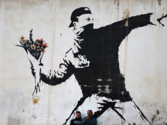 Foto de grafite na cor preta sobre um muro claro. O desenho retrata um homem com boné e rosto coberto segurando um buquê de flores, em um gesto de quem se prepara para lançar o objeto, semelhante ao gesto de quem lança uma granada ou um coquetel Molotov. As flores são amarelas e vermelhas.