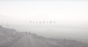 foto de uma estrada de terra próxima ao mar. duas pessoas caminham pela estrada ao fundo. acima o céu. Toda a imagem está esbranquiçada, como uma névoa. Ao centro, em letras maiúsculas, a palavra Pilgrims