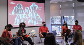 Foto de seis diretores da ECA Jr., homens e mulheres, sentados em frente à projeção com uma foto da equipe gestora. Eles vestem a camiseta vermelha da empresa.  No canto inferior da imagem, alguns estudantes assistem a apresentação.  Todos usam máscaras.