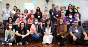 Foto de grupo de funcionárias e funcionários da ECA posando; à frente, as funcionárias estão sentadas; atrás delas outras funcionárias estão sentadas em carteiras escolares; ao fundo, em pé, os demais funcionários e funcionárias, além dos dois ministrantes do curso.