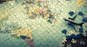 Quebra cabeça do mapa mundi. O quebra cabeça é colorido, com predominio da cor azul. As peças do mapa estão quase todas encaixadas e mostra principalmente o continente africano e a américa latina. sobre o mapa, um pequeno avião de brinquedo.