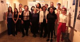 Fotografia dos vencedores do concurso, durante a cerimônia de premiação. Na imagem, 16 pessoas estão reunidas, posando e sorrindo, olhando em direção à câmera. O espaço conta com um piso marrom e paredes brancas