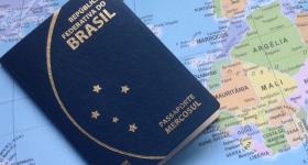 Foto de um passaporte brasileiro em cima de um mapa mundi. A capa do documento é azul marinho e tem detalhes em dourado. No canto superior está escrito “República Federativa do Brasil” e, no canto inferior, “Passaporte Mercosul”. Ao centro, há cinco estrelas posicionadas como a constelação Cruzeiro do Sul. No mapa, é possível ver os países do oeste africano e a Península Ibérica.