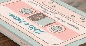 Foto de um livro sobre uma superfície de madeira. Ele tem capa azul clara com a ilustração de uma fita k7 na vertical e em tons de rosa, ocupando quase toda a capa. Está escrito em letras de forma, com fonte de estilo manuscrito, em azul, João e Maria, no topo da fita e, na parte debaixo dela, está escrito Pequeno tratado amoroso, seguido do nome do autor, Jean Pierre Chauvin, ambos em fonte preta. Na lombada do livro, também consta o nome do autor em fonte preta sobre faixa rosa.