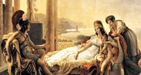 ​ Pintura clássica. De um lado, Enéas, um homem branco em uma armadura e capacete, está sentado em uma cadeira, gesticulando em conversa. Ao seu lado, Dido, uma mulher branca de cabelos longos e castanhos, está reclinada em um divã. Ela usa um vestido longo e branco e um adorno na cabeça. Ela está abraçada a uma criança, de pé, ao seu lado. Uma outra mulher, usando um vestido longo azul, está de pé, apoiada no encosto do divã. A cena se passa em um terraço com colunas. Ao fundo, há montanhas e a praia